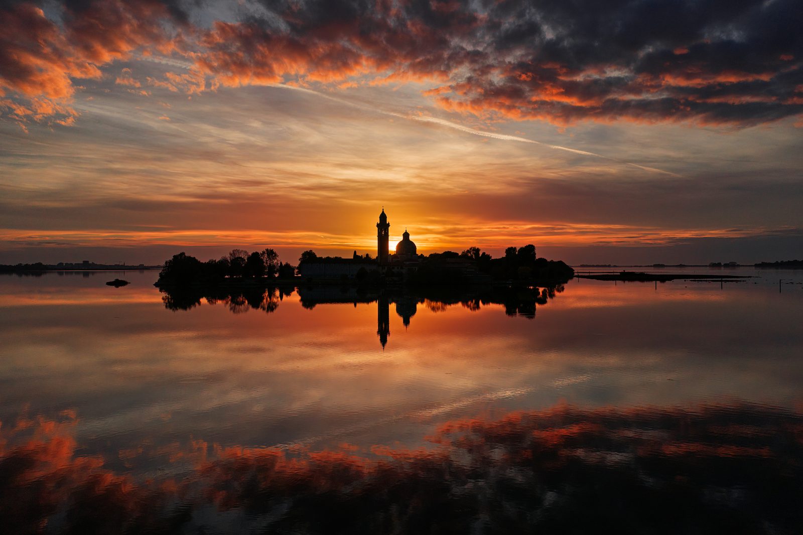 L’isola di Barbana in controluce al tramonto, con il cielo arancione riflesso nell’acqua
