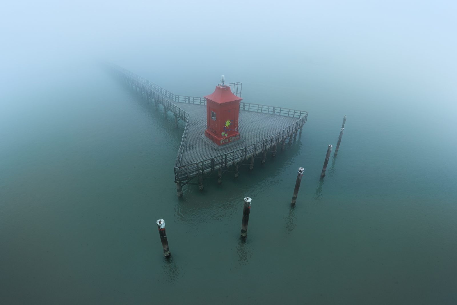 Il faro rosso di Lignano nella nebbia, al termine della passerella di legno con i pali