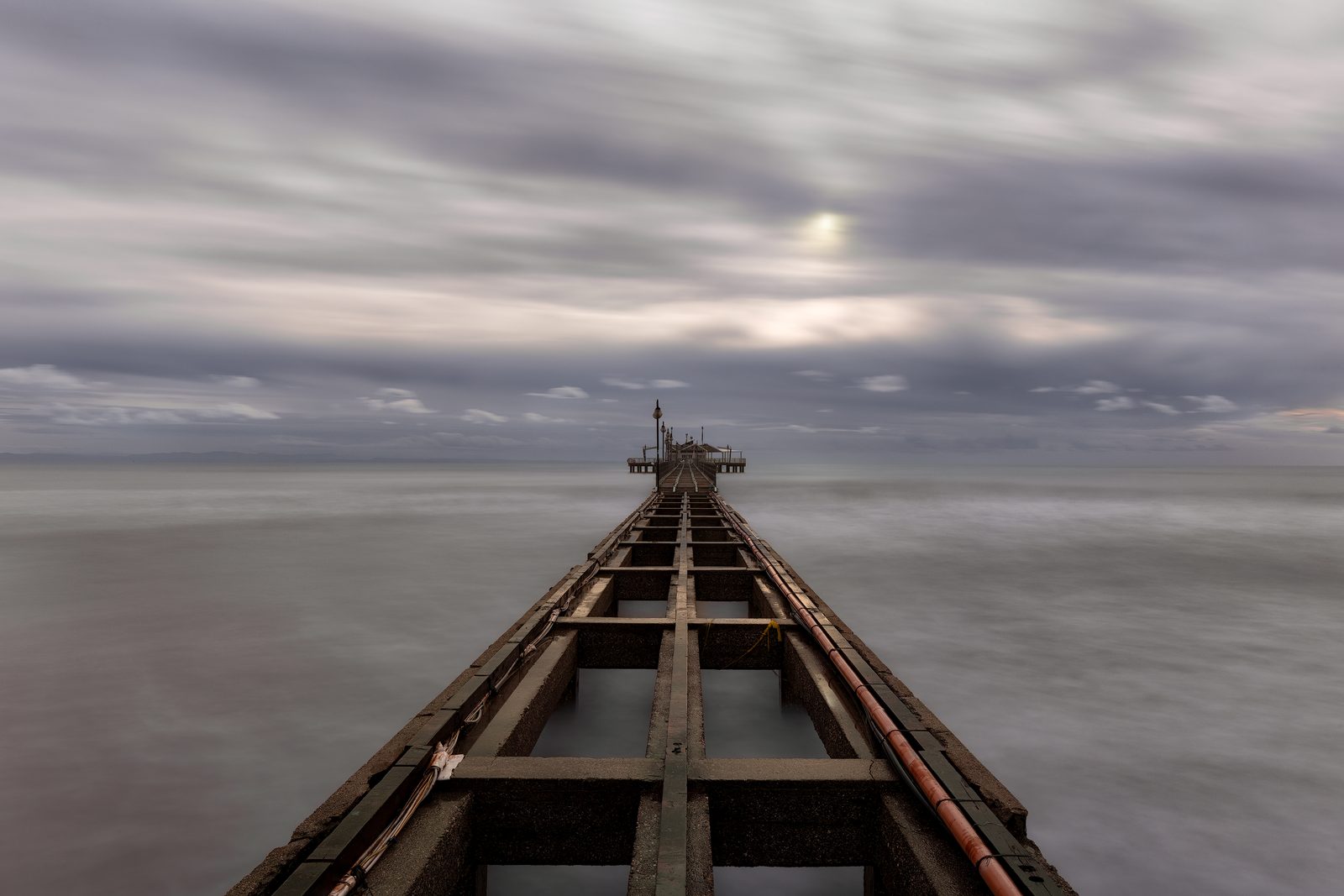 Una passerella di travi di legno che si allunga verso il mare sotto un cielo grigio