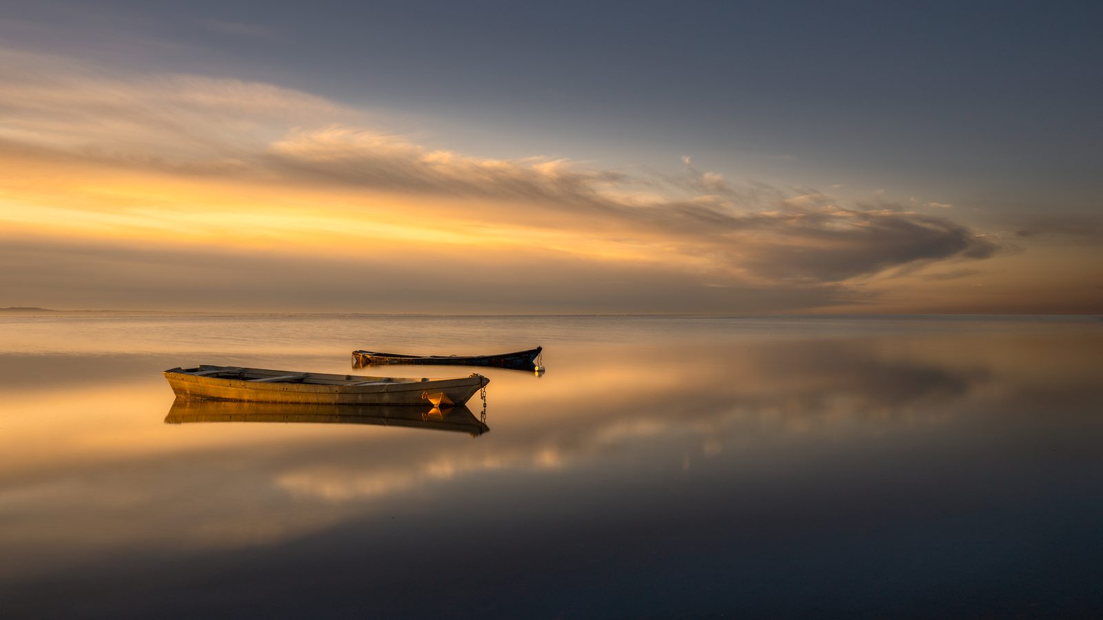 Due barche ferme sull’acqua a specchio, al tramonto